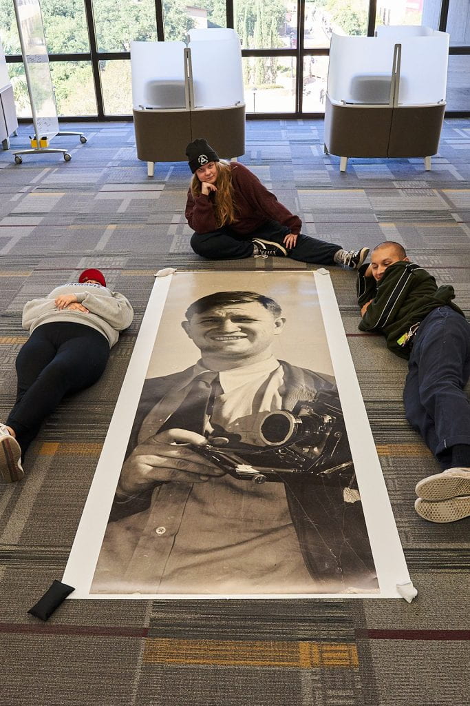 Two students on side and one student sitting above a long, narrow print on the floor